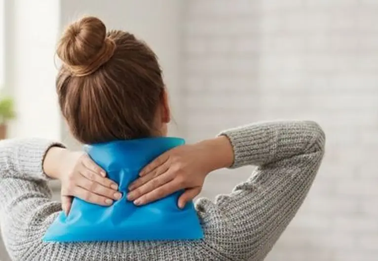 Woman applying a reusable blue cold pack to the back of her neck for pain relief