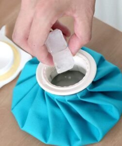 Hand placing an ice cube into the wide opening of a blue fabric ice bag