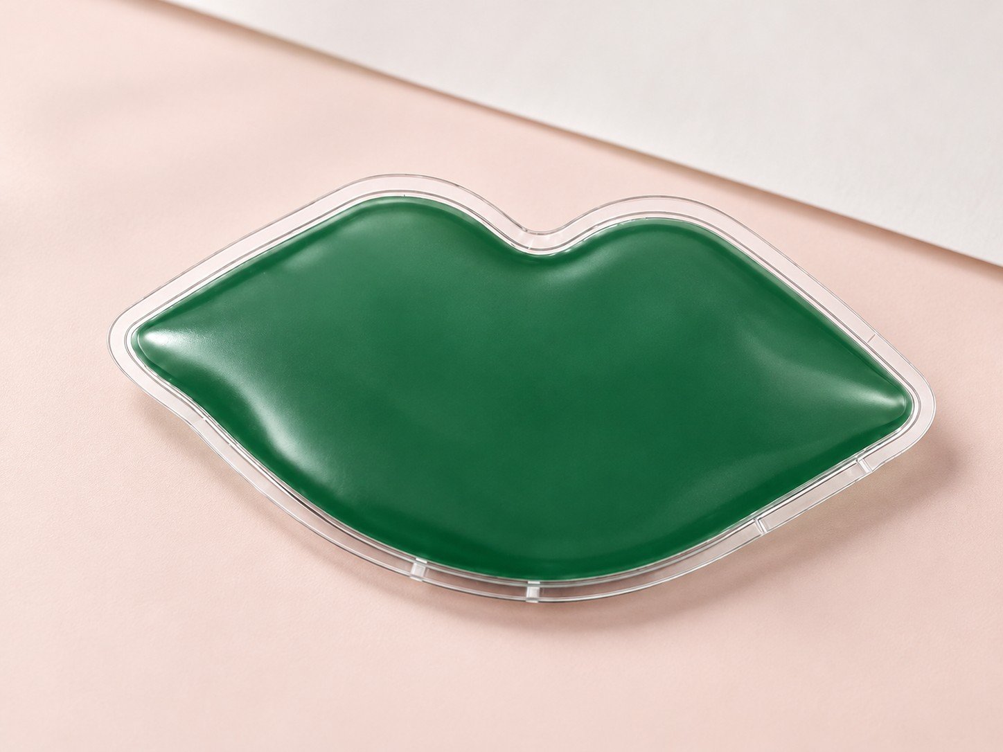 Unprinted green lip-shaped gel pouch with a clear sealed border and unobstructed central panel on a pale blush table