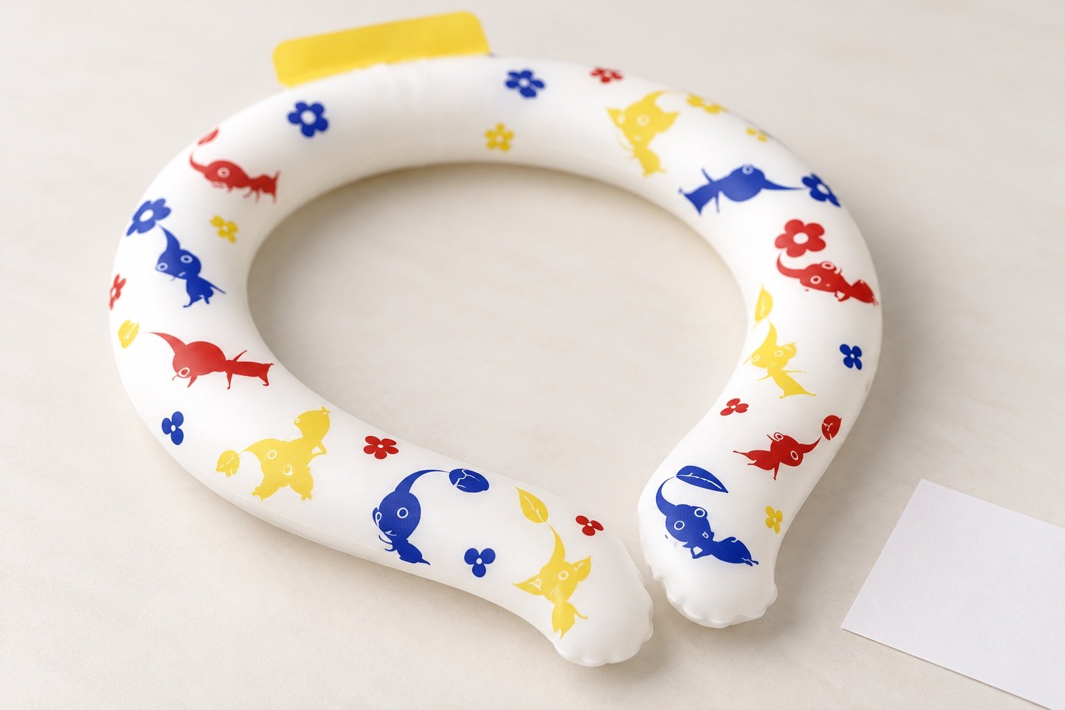 Oblique detail of a white neck ring with small multicolor fish and flower artwork and a yellow tab